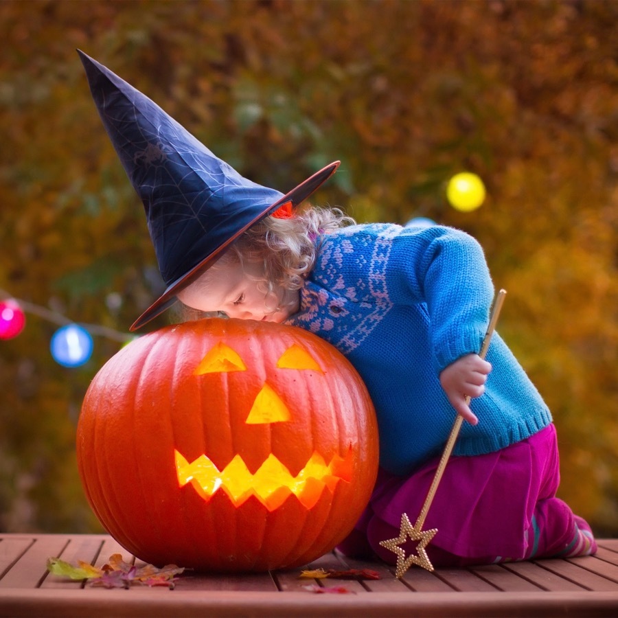 A young girl peaking into a jack-o-lantern