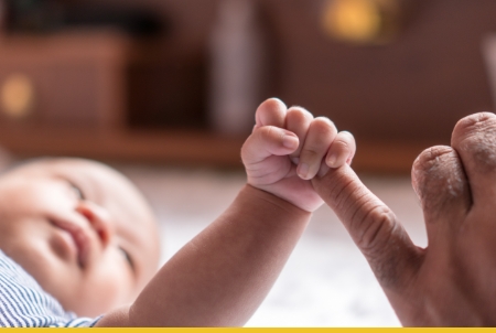 A close-up view of a baby reaching for an adult's finger