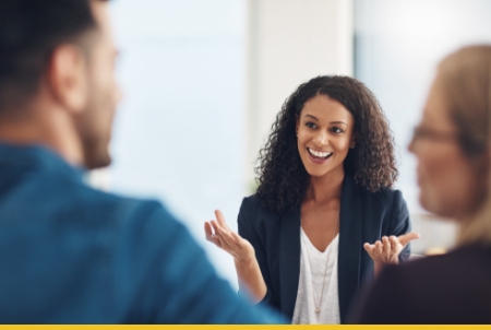 Woman with curly hair presenting to colleagues in bright office meeting room