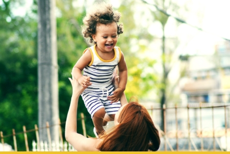 A joyful child being playfully lifted by an adult in a sunny outdoor setting.