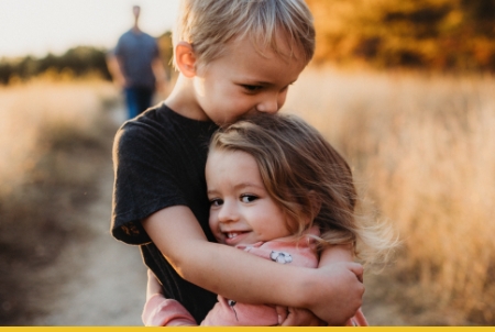 Two children hugging in a field during golden hour