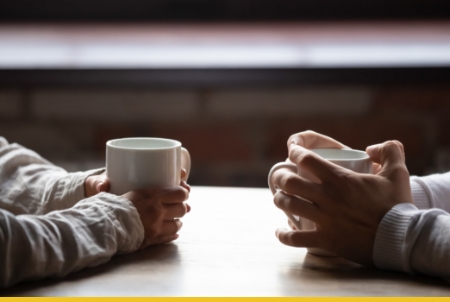 Two people holding white mugs while sitting at a wooden table
