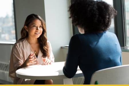 Two women engaged in a conversation at a table in a bright office setting