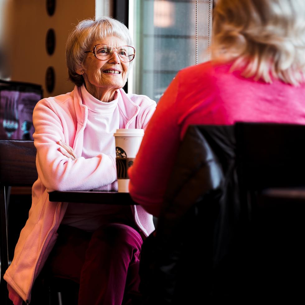 An elderly woman speaking with a younger woman at a table