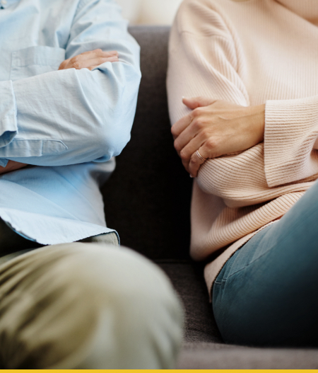 Image of a couple sitting apart on a couch with crossed arms