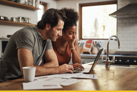 A couple collaborating on a laptop in a cozy kitchen setting.