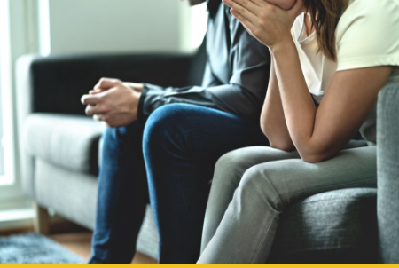 A couple sitting on a sofa with their faces in their hands