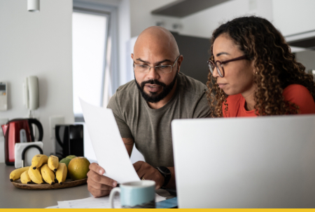 A man and a woman reviewing documents together at a kitchen table with fruits in the foreground