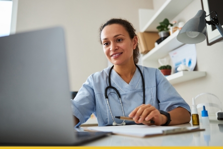Smiling female doctor with stethoscope sitting at desk with computer in medical office