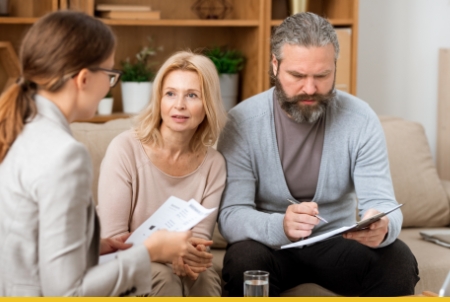 A professional consultation where a woman is discussing paperwork with a couple seated together in a cozy setting.