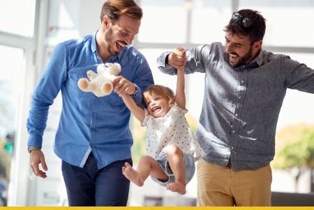 Happy family moment with two dads playing with a child in a bright setting.