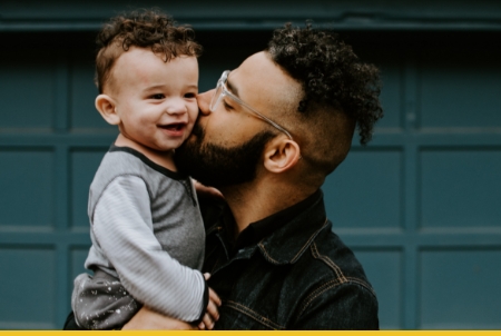 A man gently kisses a smiling baby he is holding
