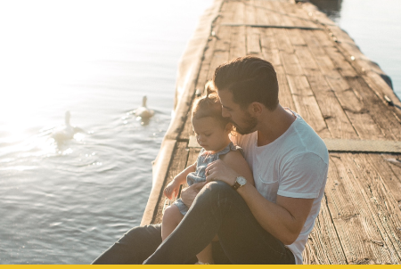 A father and daughter sitting on a wooden dock by a lake