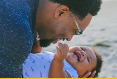 A joyful father playing with his laughing baby on the beach.