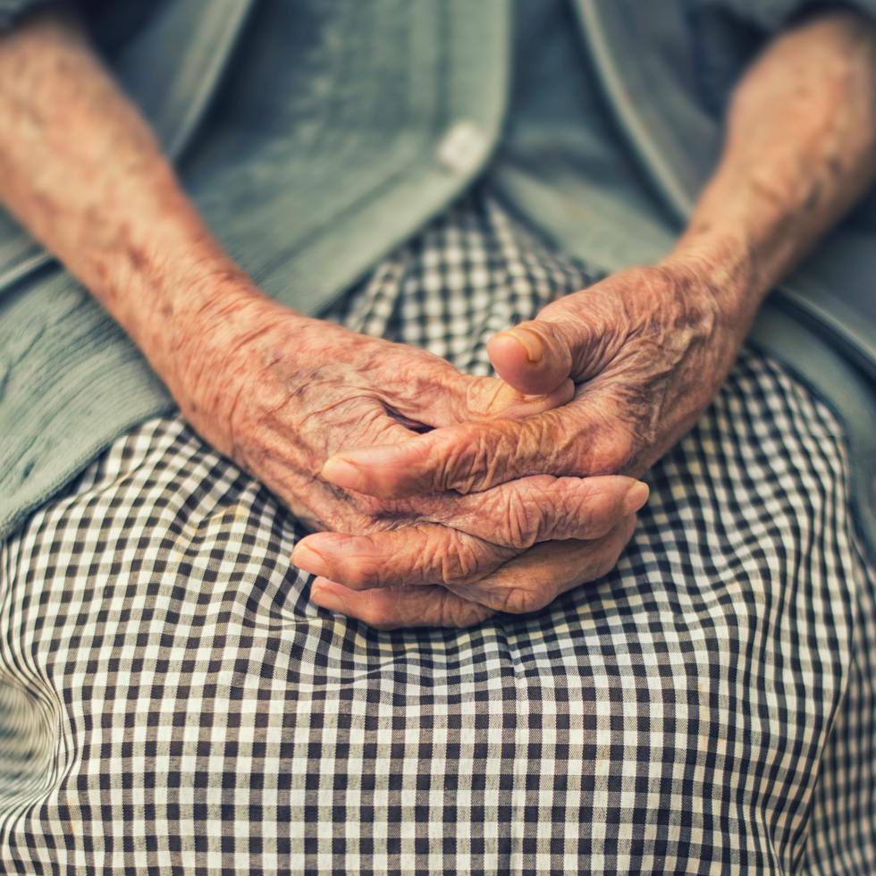 An elderly woman sitting while holder her hands
