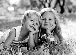 Two children smiling while lying on the grass in a black and white photograph