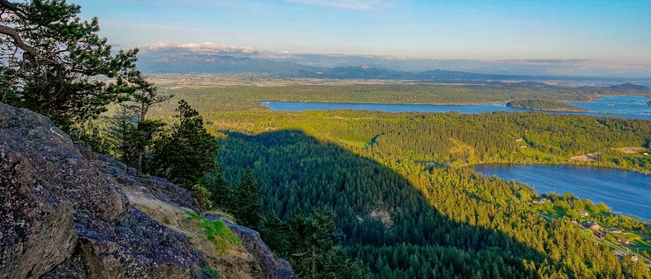 Panoramic view from rocky mountain overlook showing vast forested landscape with multiple blue lakes and distant mountain ranges