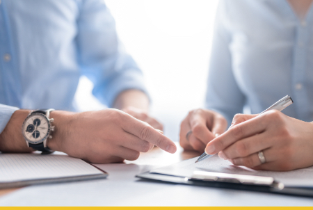 A close-up image of two hands engaged in a discussion while one hand points at a document and the other holds a pen